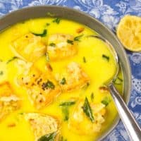 Coconut Fish Curry (Kerala Molee) Served in a pottery bowl garnished with fried curry leaves and a wedge of lemon.