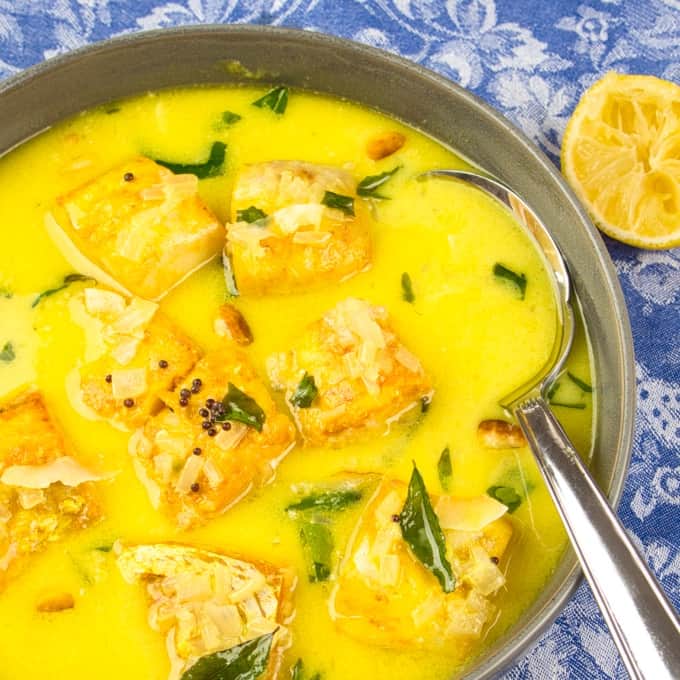 Coconut Fish Curry (Kerala Molee) Served in a pottery bowl garnished with fried curry leaves and a wedge of lemon.