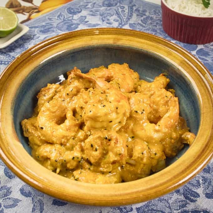 Bengali Prawn Curry (Chingri Posto) Served in a beautiful gold and blue dish with rice and lime on the side.