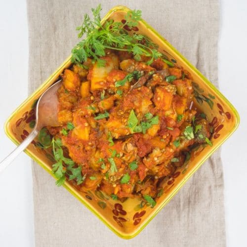 Roasted Eggplant Curry (Baingan Bharta) Beautiful redish orange eggplant curry in a square gold serving bowl garnished with a dusting fresh green cilantro