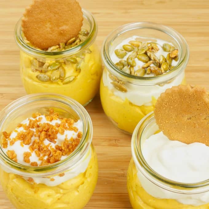 Cardamom Pumpkin Cheesecake (No-Bake) four small jars of cheesecake all garnished differently: with candied pumpkin seeds, whipped cream and whole ginger cookies