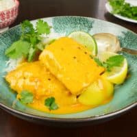 Served atop a bowl of rice, garnished with lemon wedges and a sprinkling of fresh cilantro.