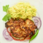 Skinless, boneless tandoori chicken thighs on a bed of bell peppers with a side of turmeric yellow rice.
