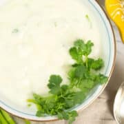 Simple raita garnished with a frilly bunch of cilantro and accompanied by sliced shallot.