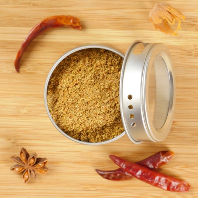 A spice tin filled with spice powder with whole spices keeping it company.