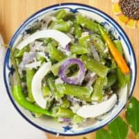 Served in a blue and white bowl garnished with large coconut chips and orange green small chilies.