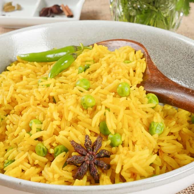 Served with a wooden spoon and garnished with whole spices, green peas, and fresh chilies.