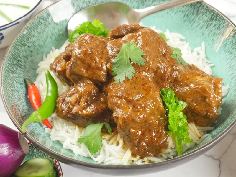 Red Beef Curry (Goan) Served on a bed of basmati rice with fresh chillies and a flutter of fresh cilantro leaves.