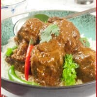 Red beef curry served on a bed of basmati rice with fresh chillies and a flutter of fresh cilantro leaves.