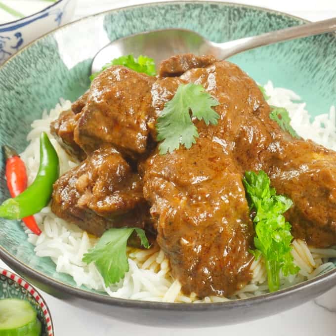 Red beef curry served on a bed of basmati rice with fresh chillies and a flutter of fresh cilantro leaves.