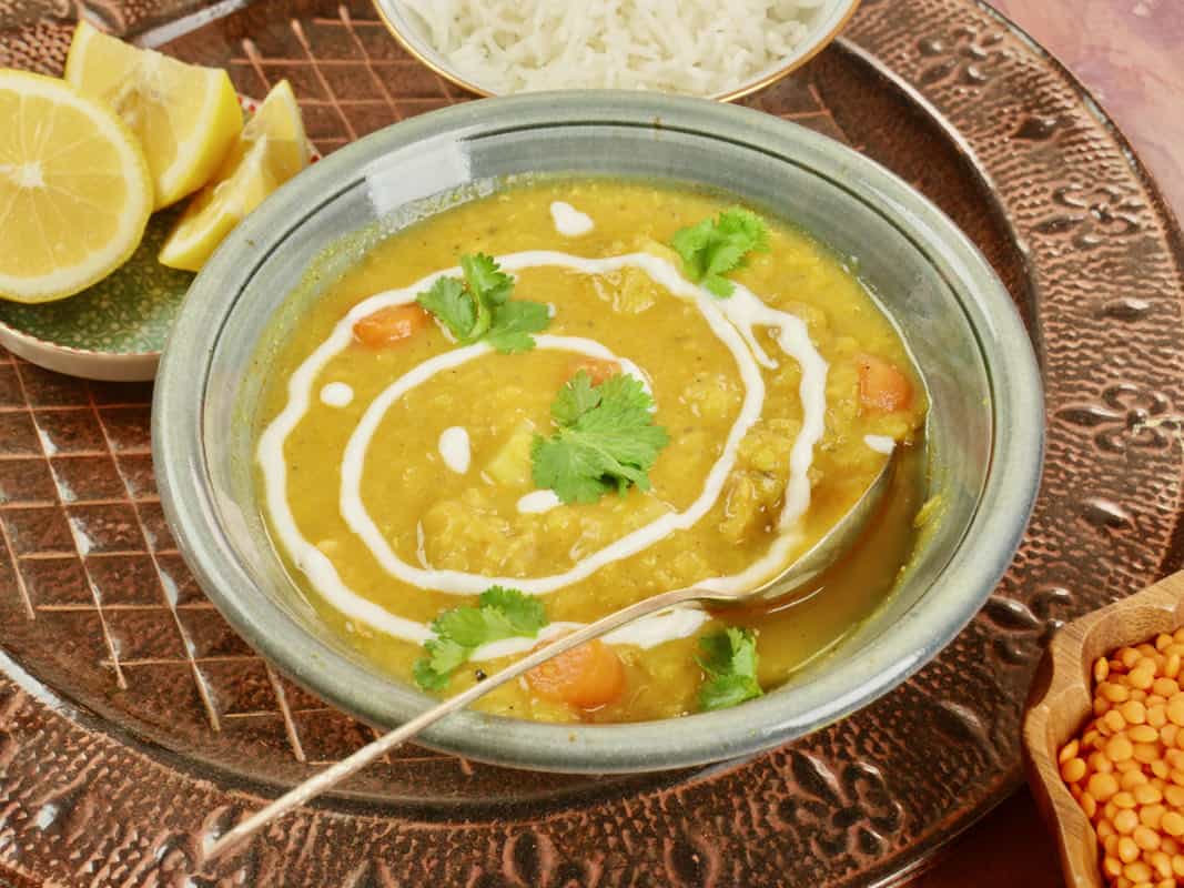 Glorious Chicken Mulligatawny Soup served with lemon slices, a bowl of rice, garnished with a drizzle of yogurt and a flutter of fresh cilantro.