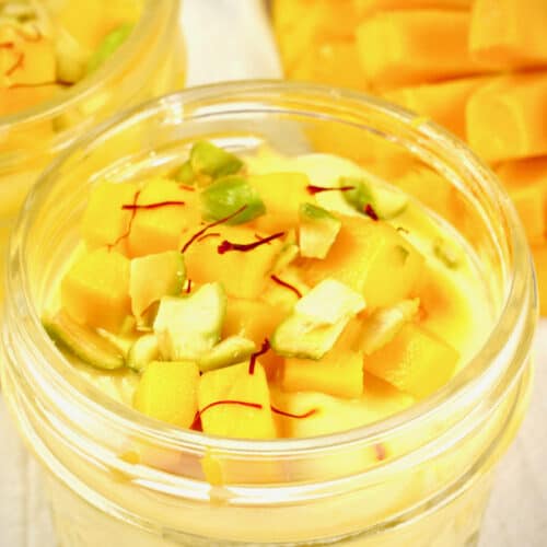 Mango fruit custard served in small jars garnished with chopped pistachios and saffron.