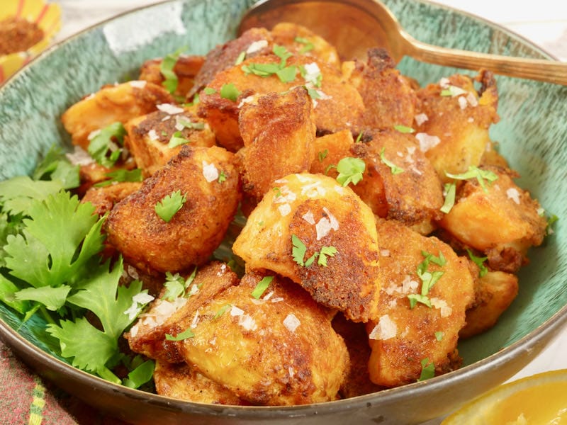 Spiced Crunchy Roasted Potatoes Served in a dish and garnished with coarse salt and a flurry of chopped cilantro.