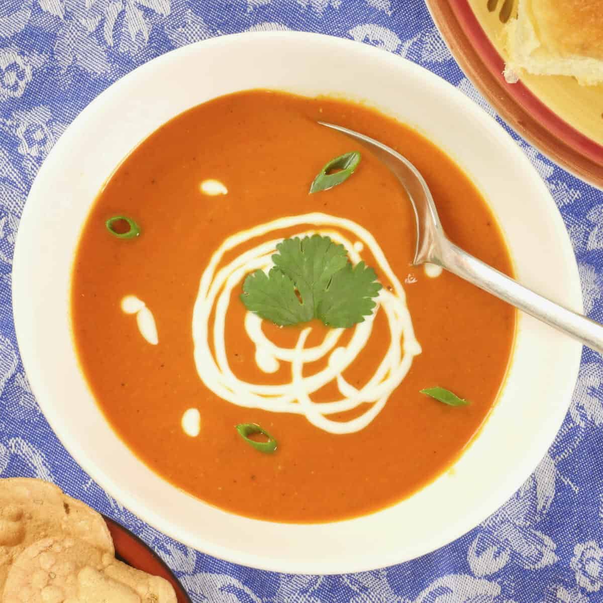 Indian Spiced Tomato Soup ~ Served in a scalloped white bowl, garnished with yogurt and a flurry of chopped cilantro.