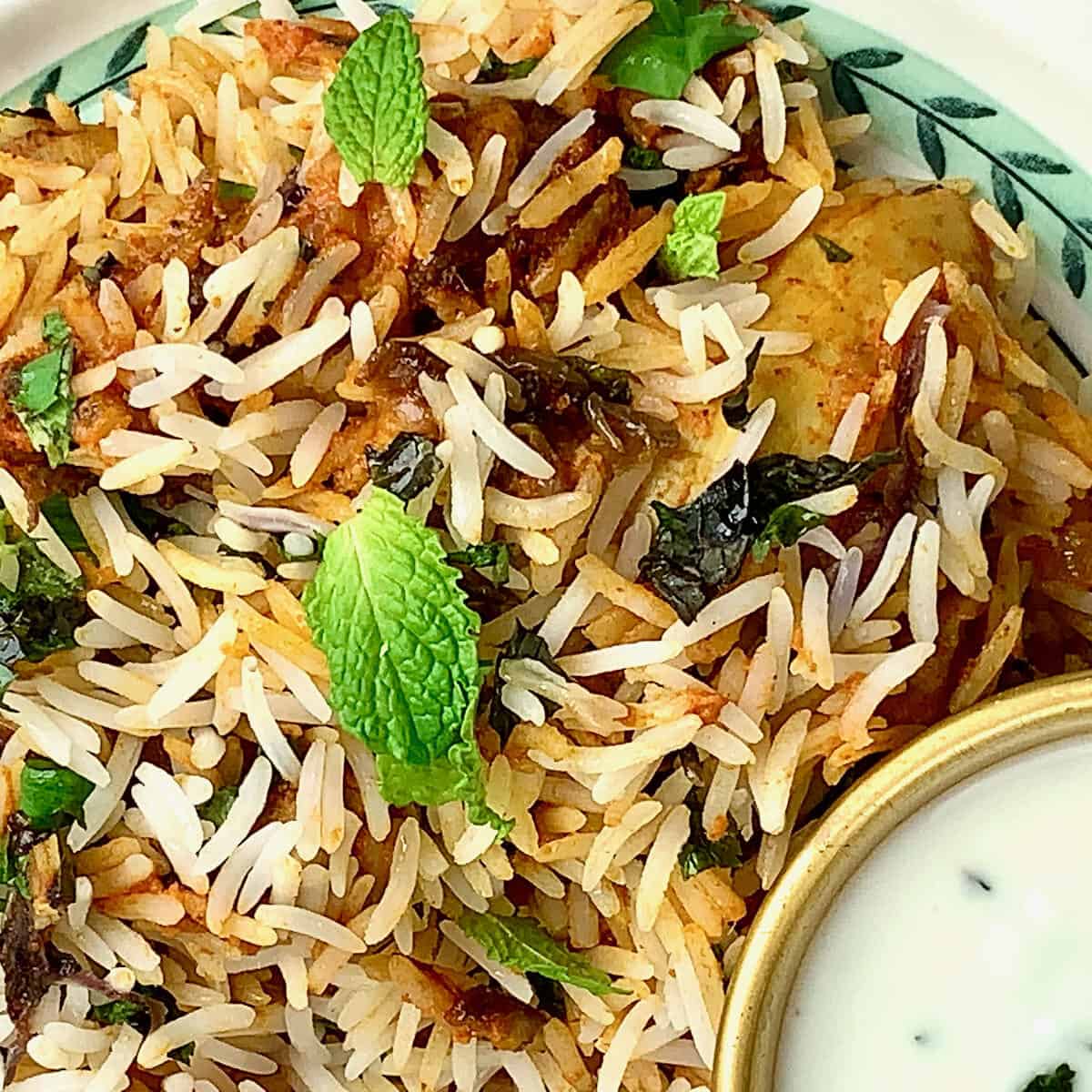 Tandoori Chicken Tikka Biryani served on a pretty plate with a flutter of fresh herbs and a side of raita.